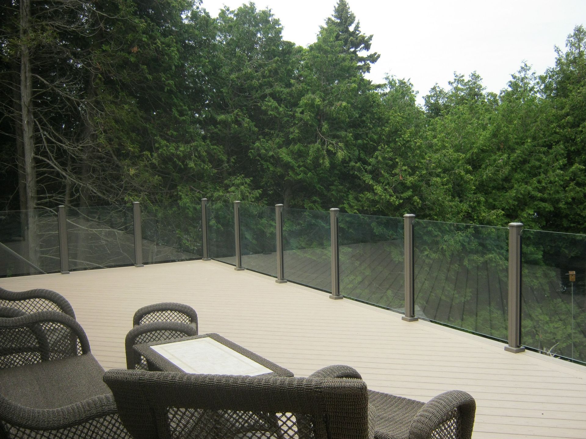 A deck with wicker furniture and a glass railing by Premier Decks & Awnings