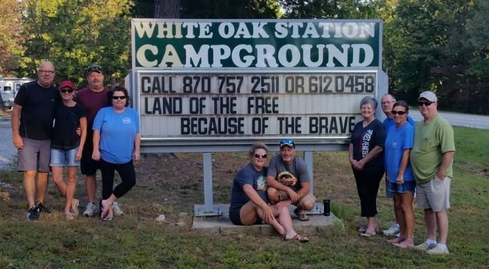 Group of people posing in front of a White Oak Station Campground sign at dusk.