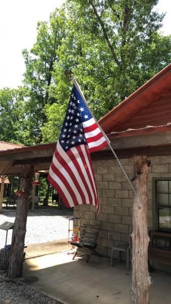 American flag hanging from a rustic porch with stone wall and trees in the background