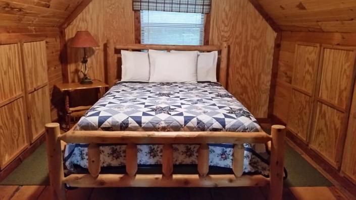 Wood-paneled bedroom with a wooden bed, white pillows, and blue-gray quilt centered beneath a window.