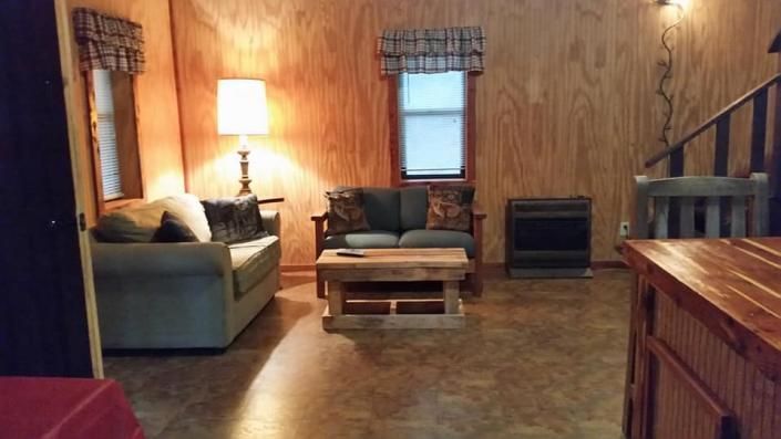 Cozy cabin living room with couch, coffee table, lamp, and stairs on the right