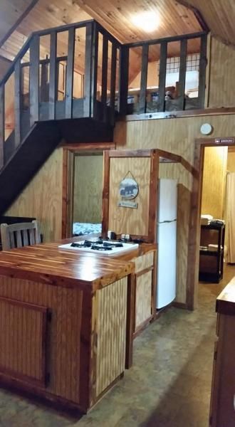 Rustic kitchen with wood-paneled walls, loft railing, and white refrigerator