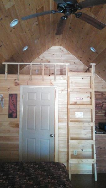 Loft room with a white door, wooden ladder, ceiling fan, and unfinished wood walls and ceiling.