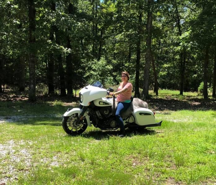 Person sitting on a white touring motorcycle in a grassy park with trees in the background