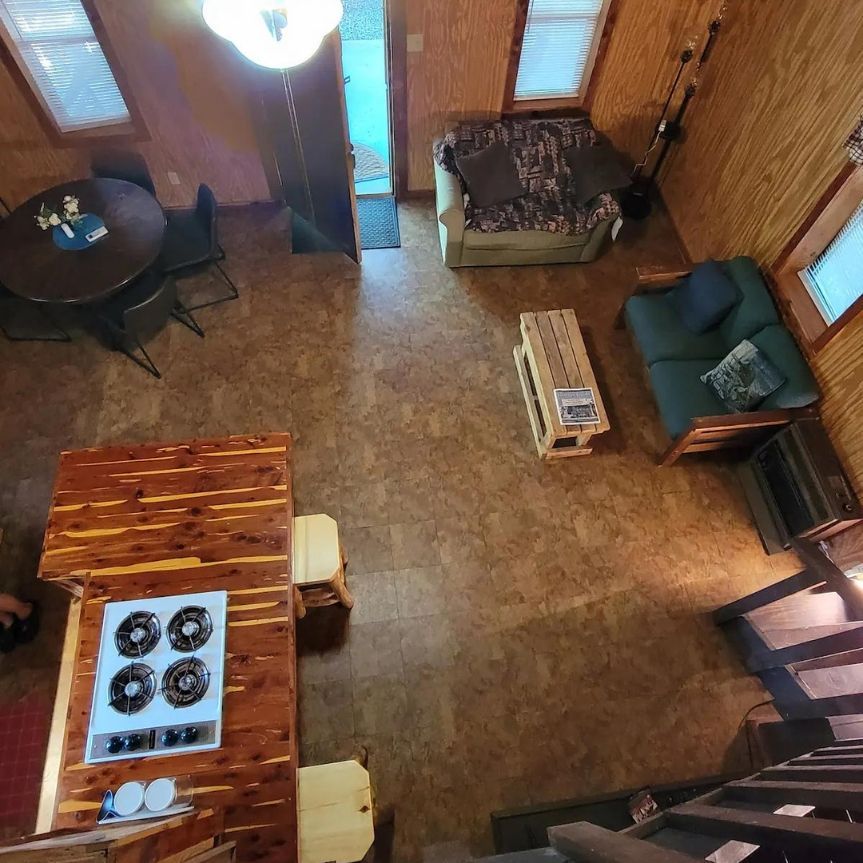 Cozy cabin interior with kitchen island, seating area, couch, and wood-paneled walls viewed from above