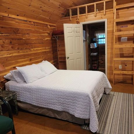 Wood-paneled bedroom with a white bed, open door, and striped rug