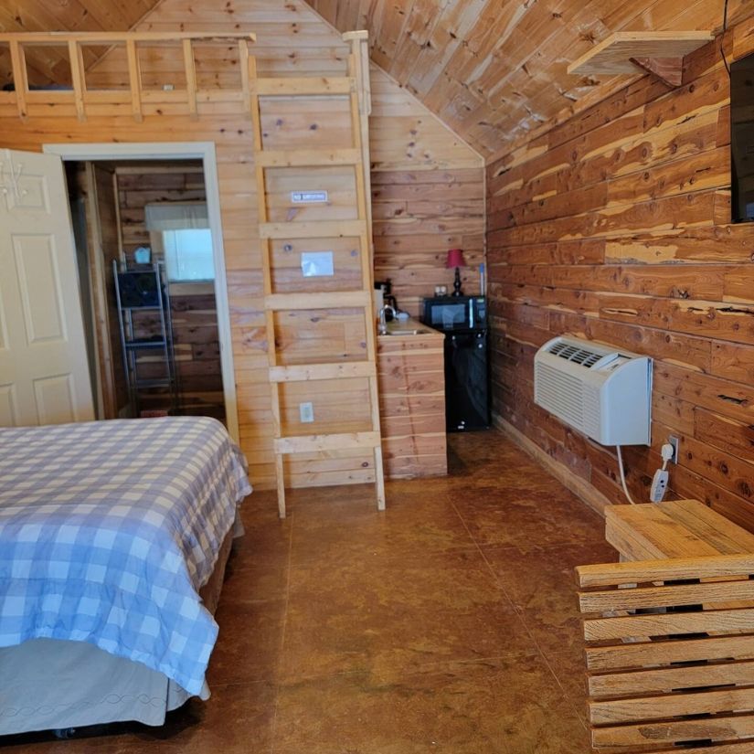 Wood-paneled cabin bedroom with bed, ladder shelf, heater, and small window seat