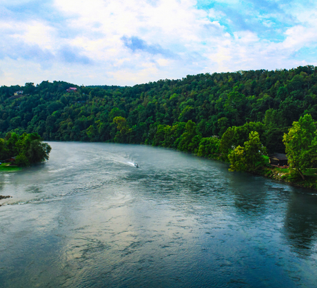 Wide river winding through green forested hills under a partly cloudy sky