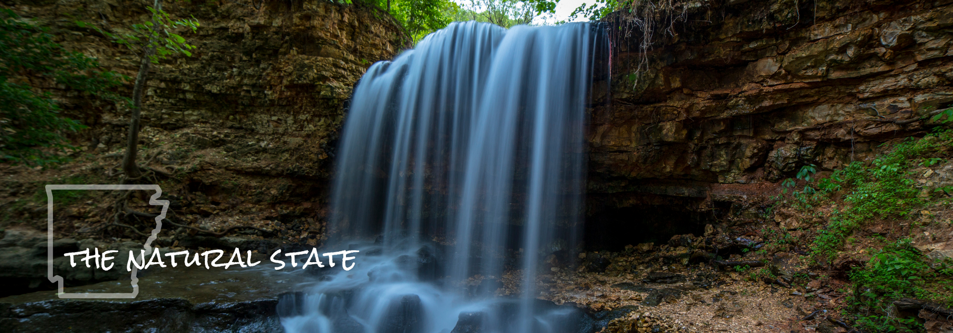 Waterfall cascading over a rocky cliff in a forest, with the text “The Natural State” at lower left