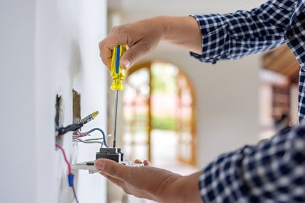 A man is fixing a light switch with a screwdriver.