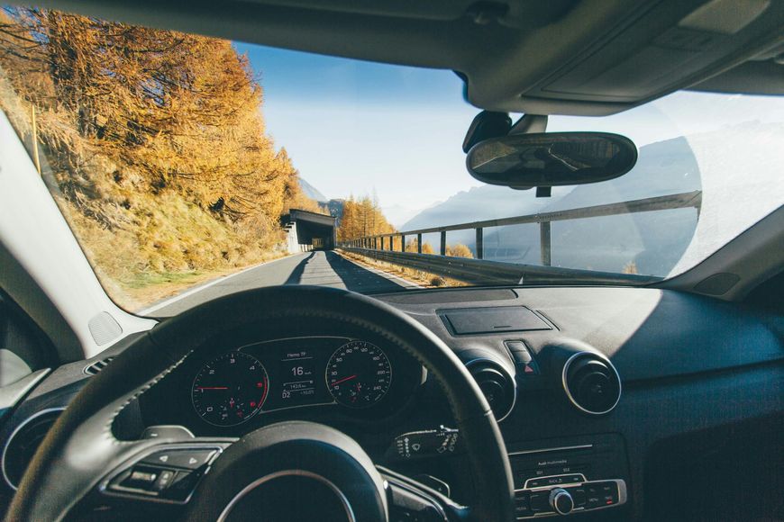 A car is driving down a road with trees in the background.