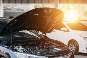 A black car with its hood open is parked next to a white car.