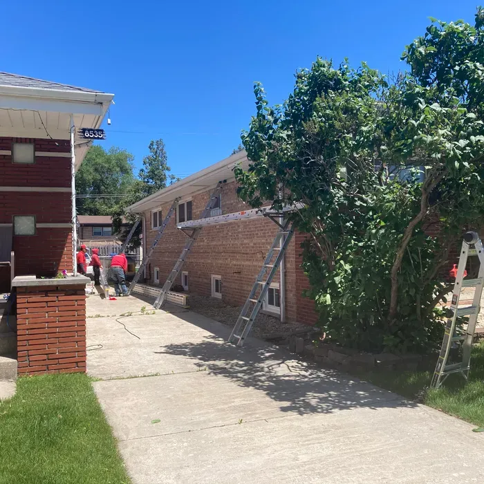 Brick building with ladder supports; workers in red shirts. Bright sunny day.