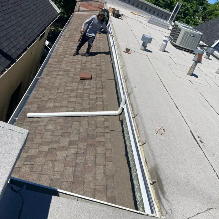 Person on a roof inspecting shingles and flat roofing.