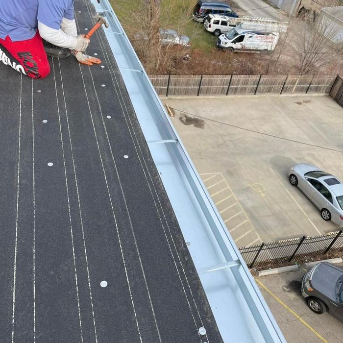 Person installing a metal gutter on a flat roof. A car park is below.