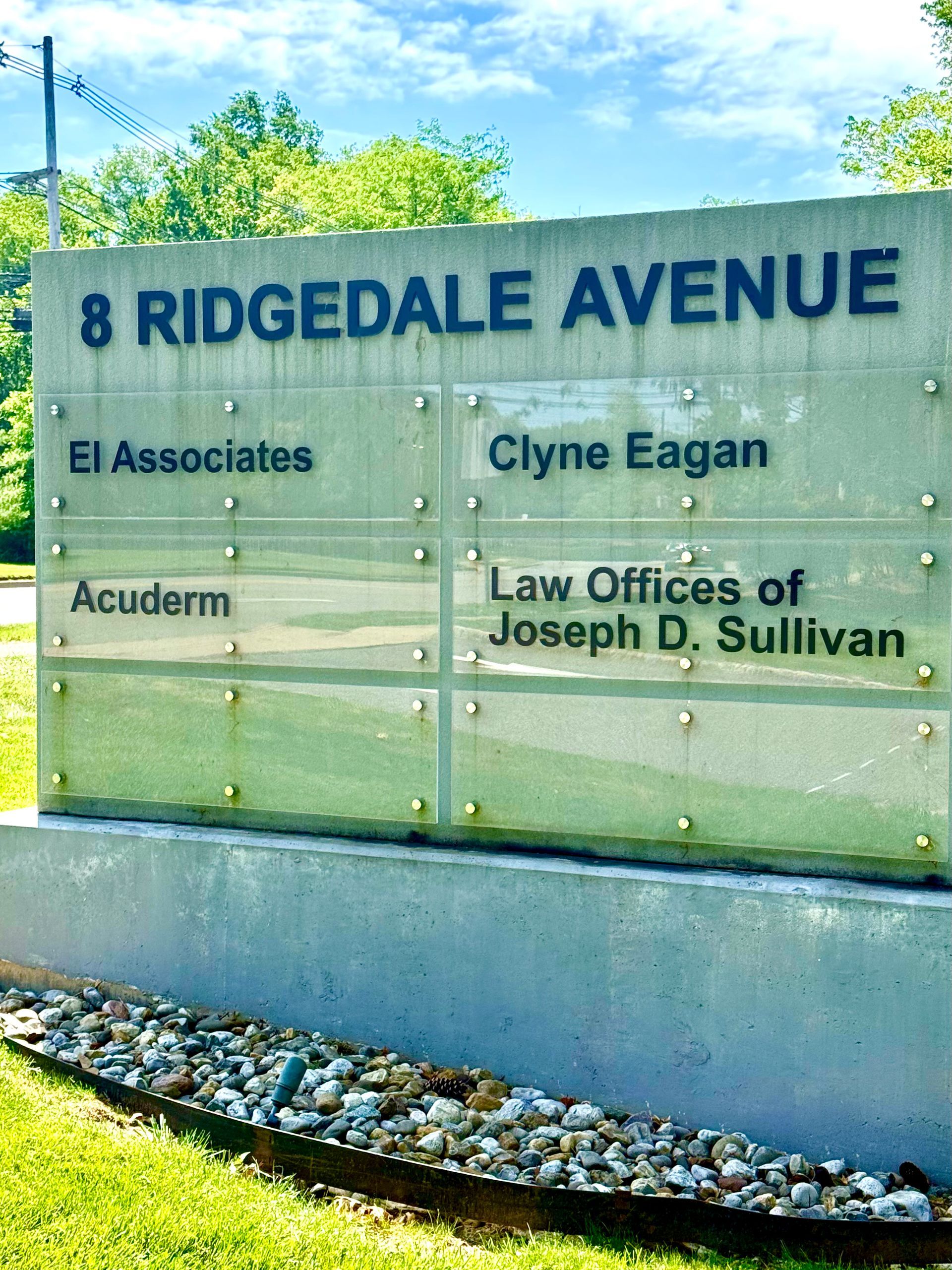 Glass sign for 8 Ridgedale Avenue listing office names against a blue sky.