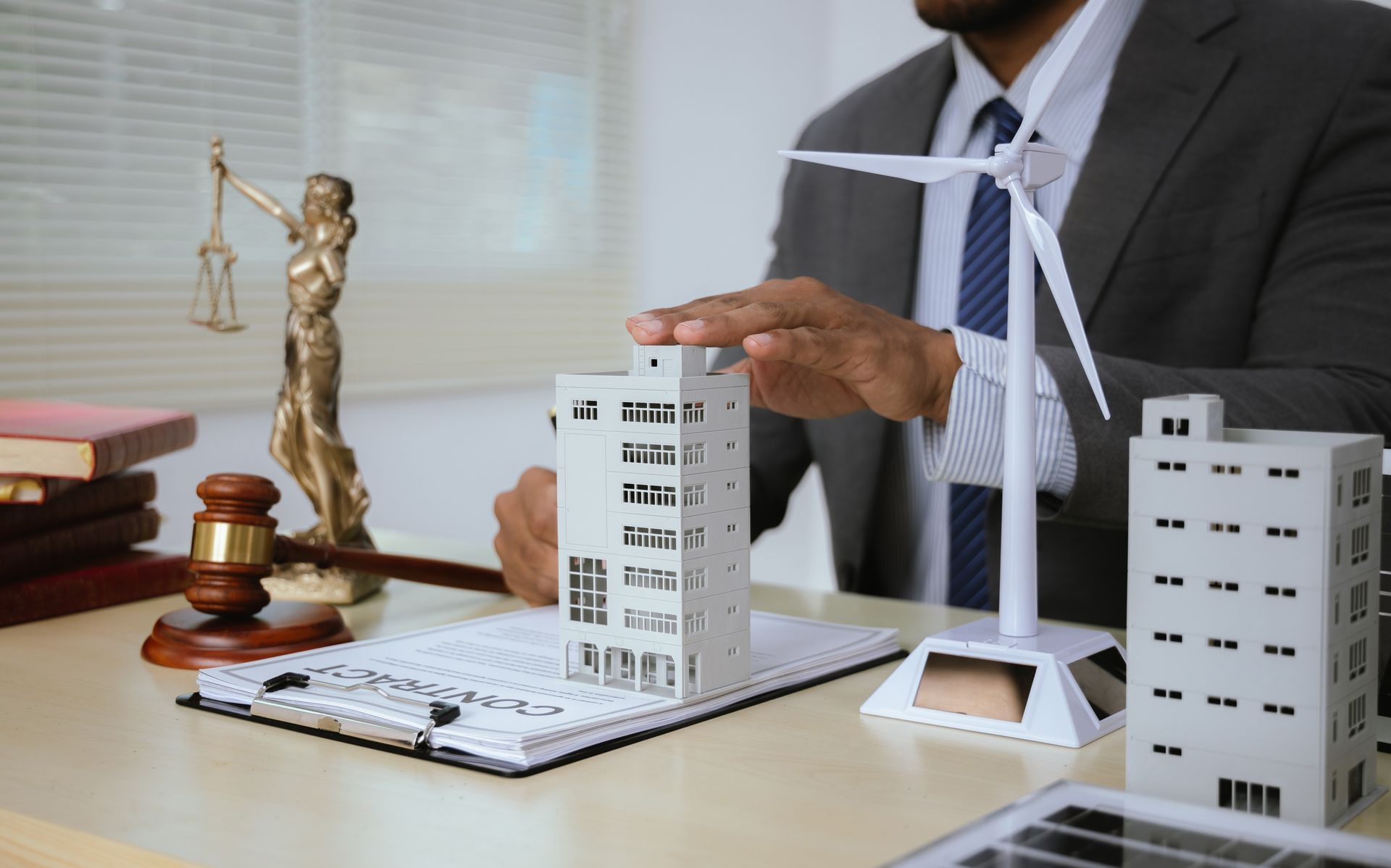 Office desk with architectural model, wind turbine, and scale of justice beside a suited professional