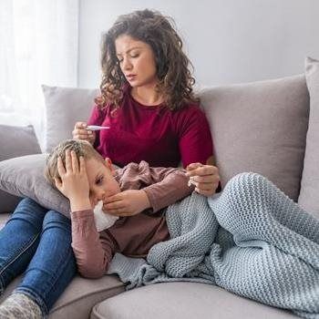 Woman checking a child’s temperature on a couch while the child rests