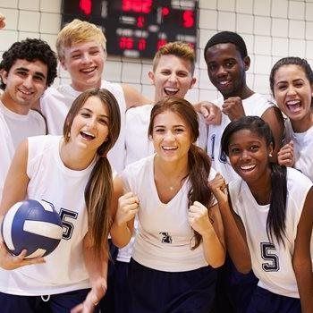 Six smiling volleyball players in white jerseys posing together in a gym