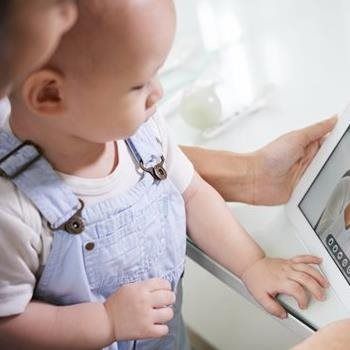 Young child in blue overalls touching a tablet screen on a bright table