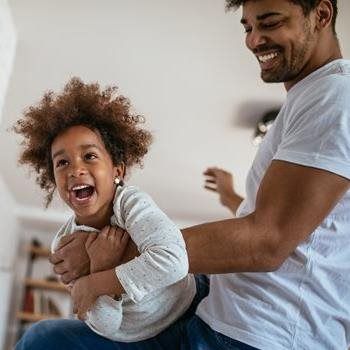 Smiling adult holding laughing child indoors in a bright room