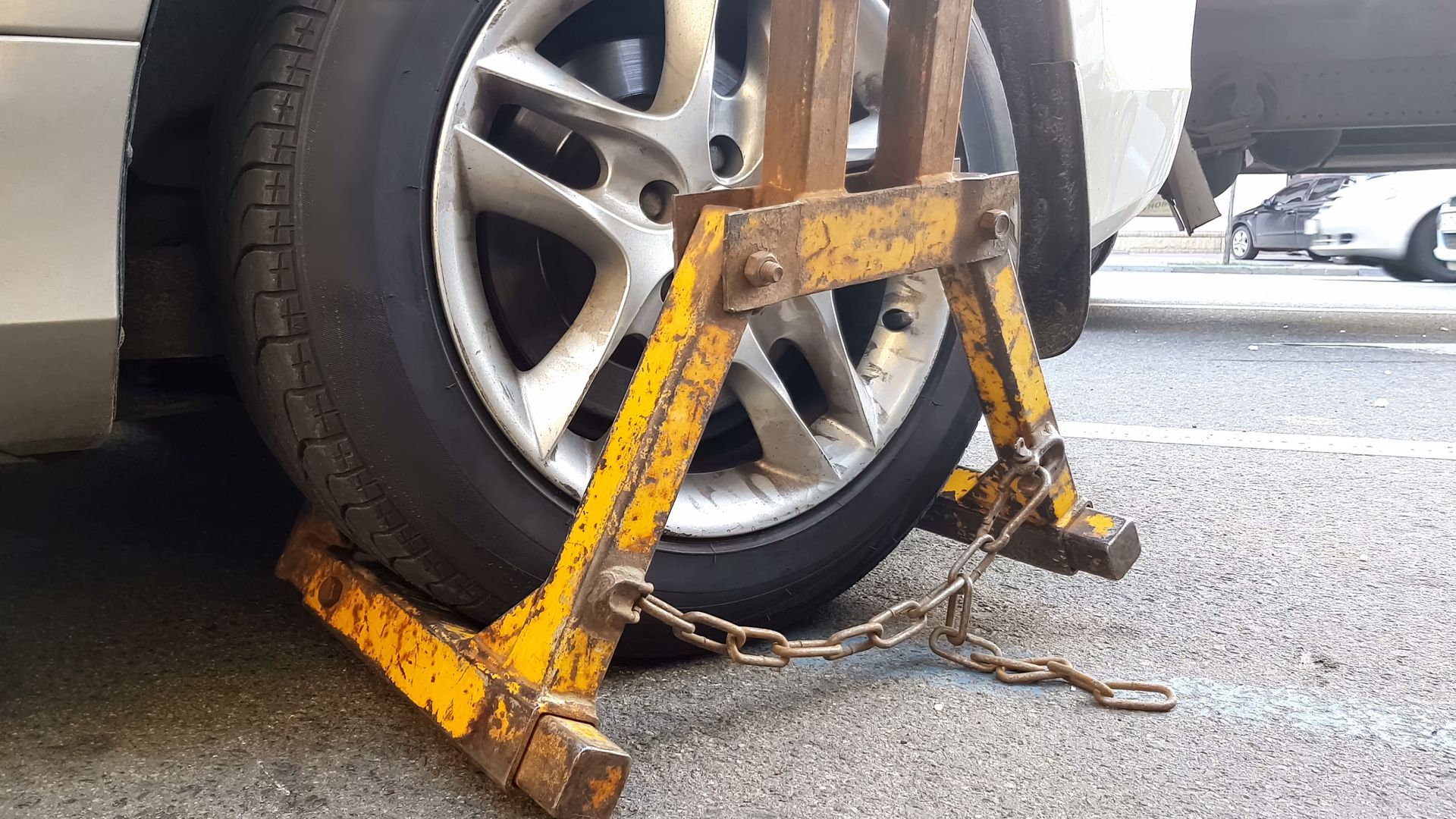 Yellow wheel clamp securing a car tire on a street beside the curb