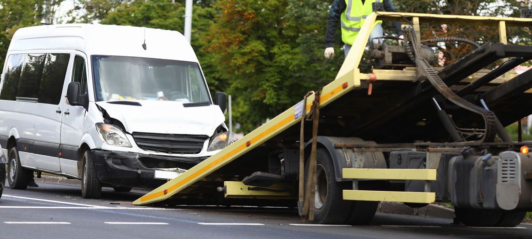 Damaged white van and tow truck with tilted ramp after roadside collision