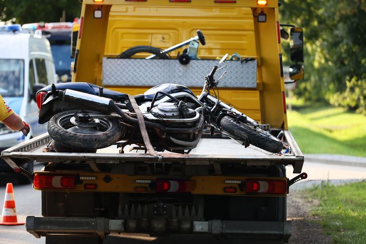 Tow truck carrying a tipped black motorcycle on a flatbed by the roadside
