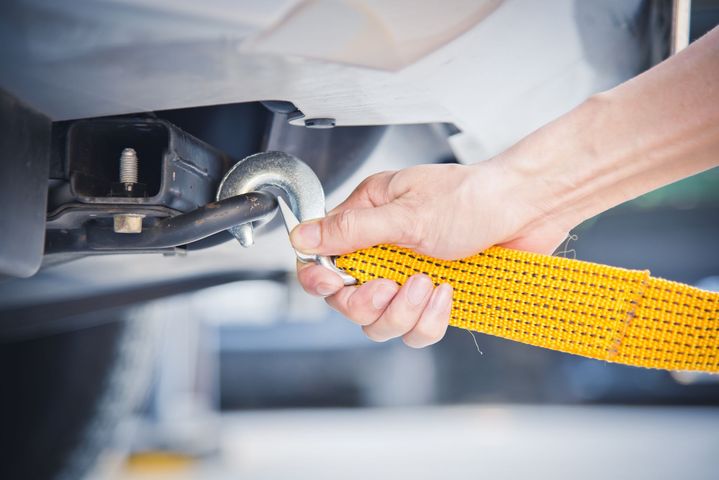 Hand tightening a yellow tow strap to a vehicle hitch under a car bumper