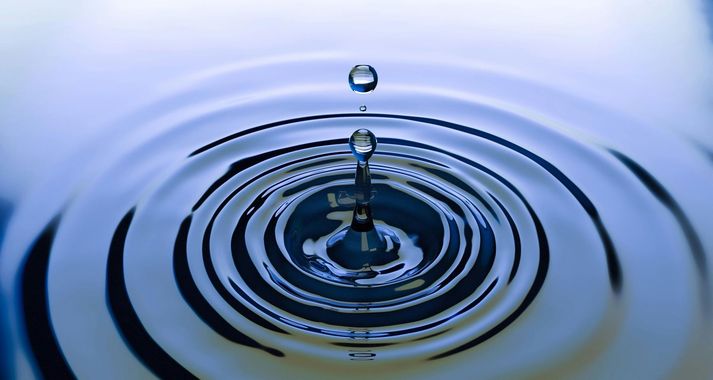 A water droplet creating ripples on a reflective surface. Light blue, circular waves.