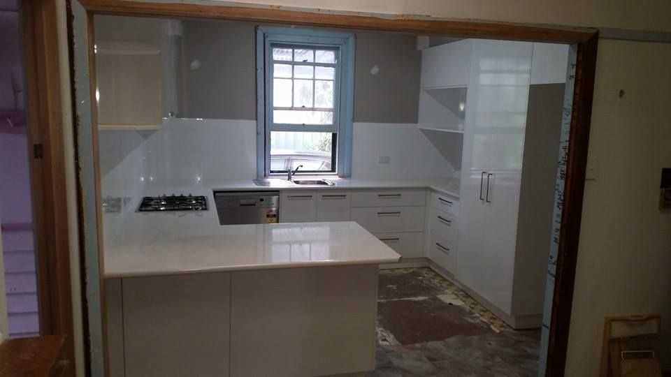 Kitchen renovation in progress, featuring white cabinets, countertops, island, and window with view.
