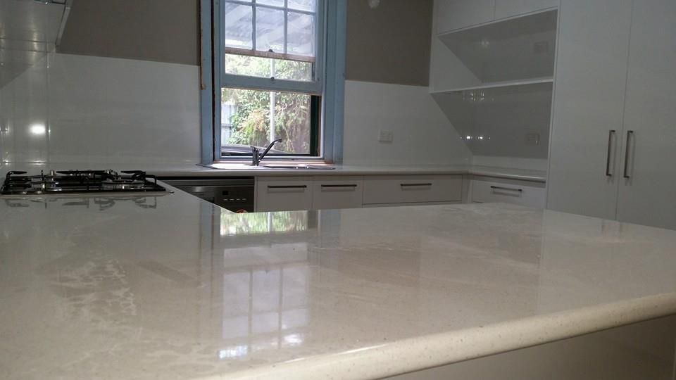 Kitchen with light-colored countertops, built-in stovetop, sink by a window, and white cabinets.
