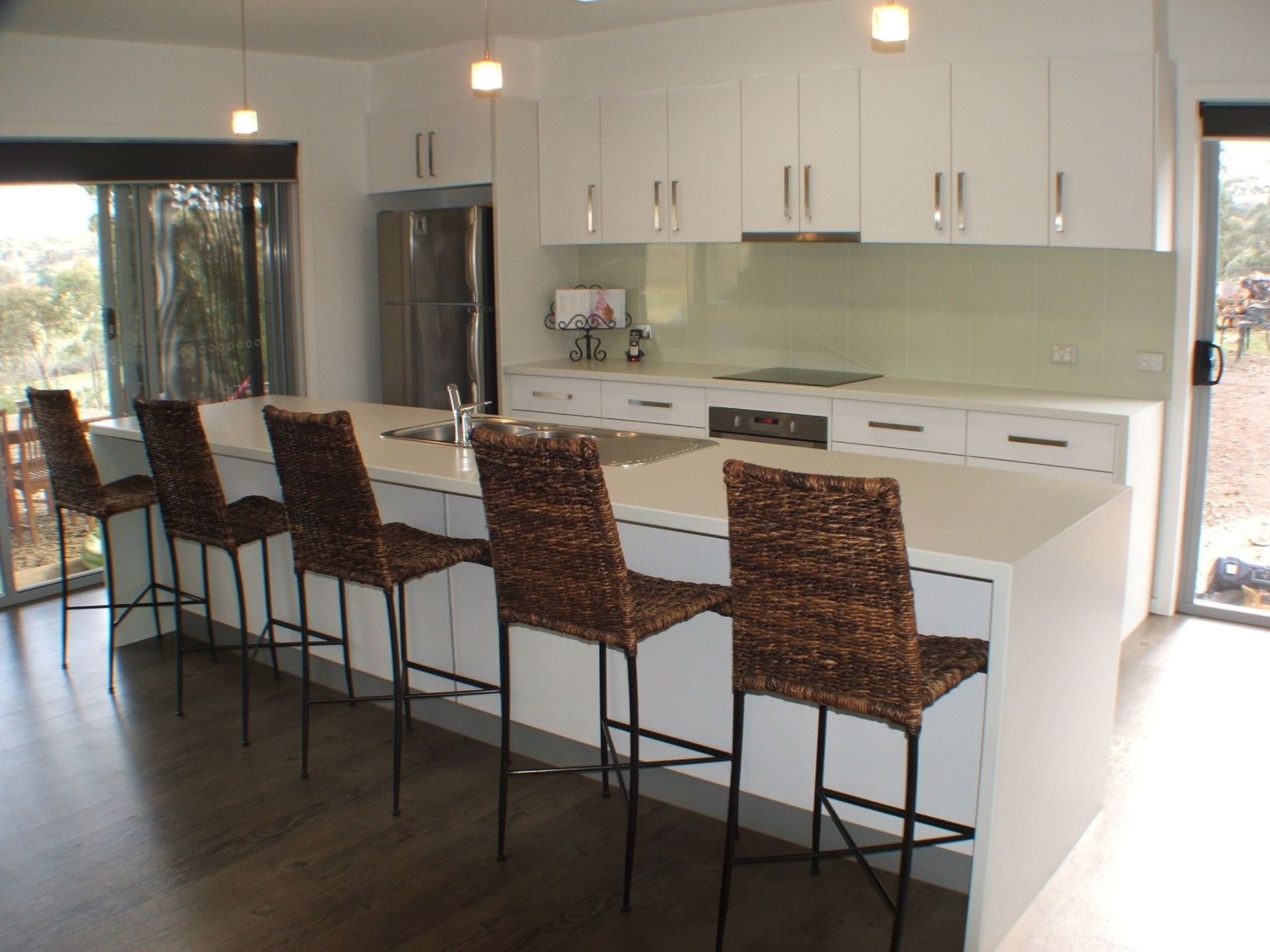 Modern white kitchen with island, seating, and woven barstools.