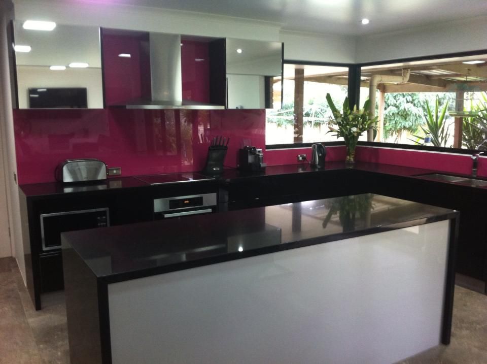 Modern kitchen with a black counter, pink backsplash, and white island.