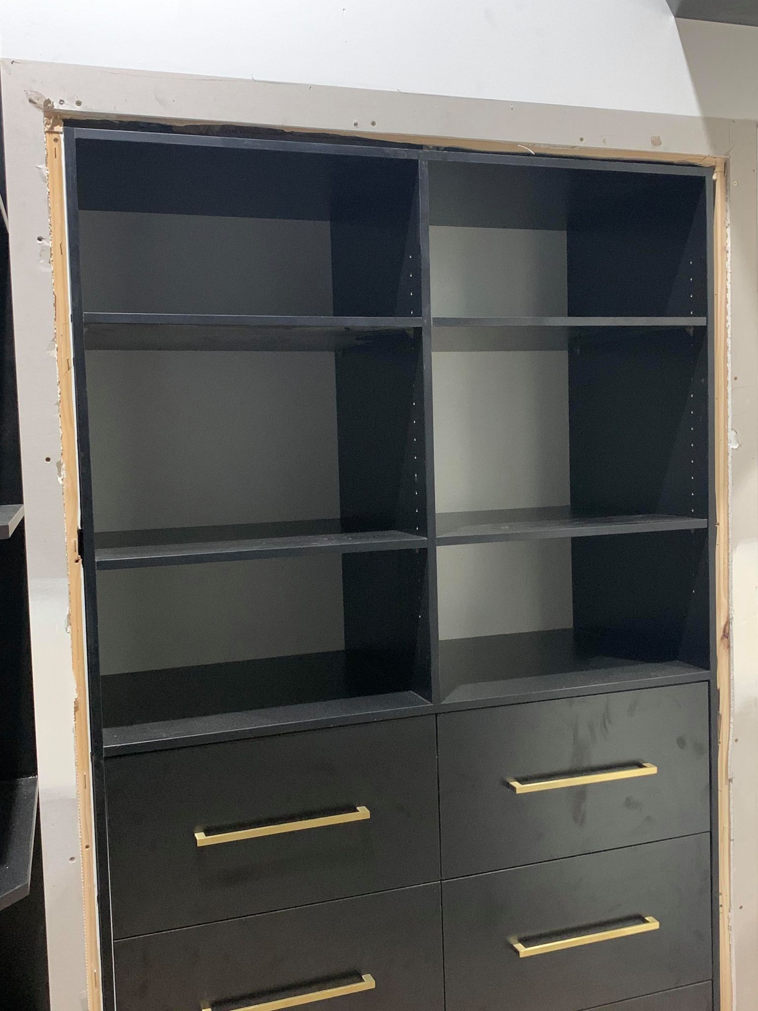 Black closet organizer with shelves and drawers, gold handles, against a white wall.