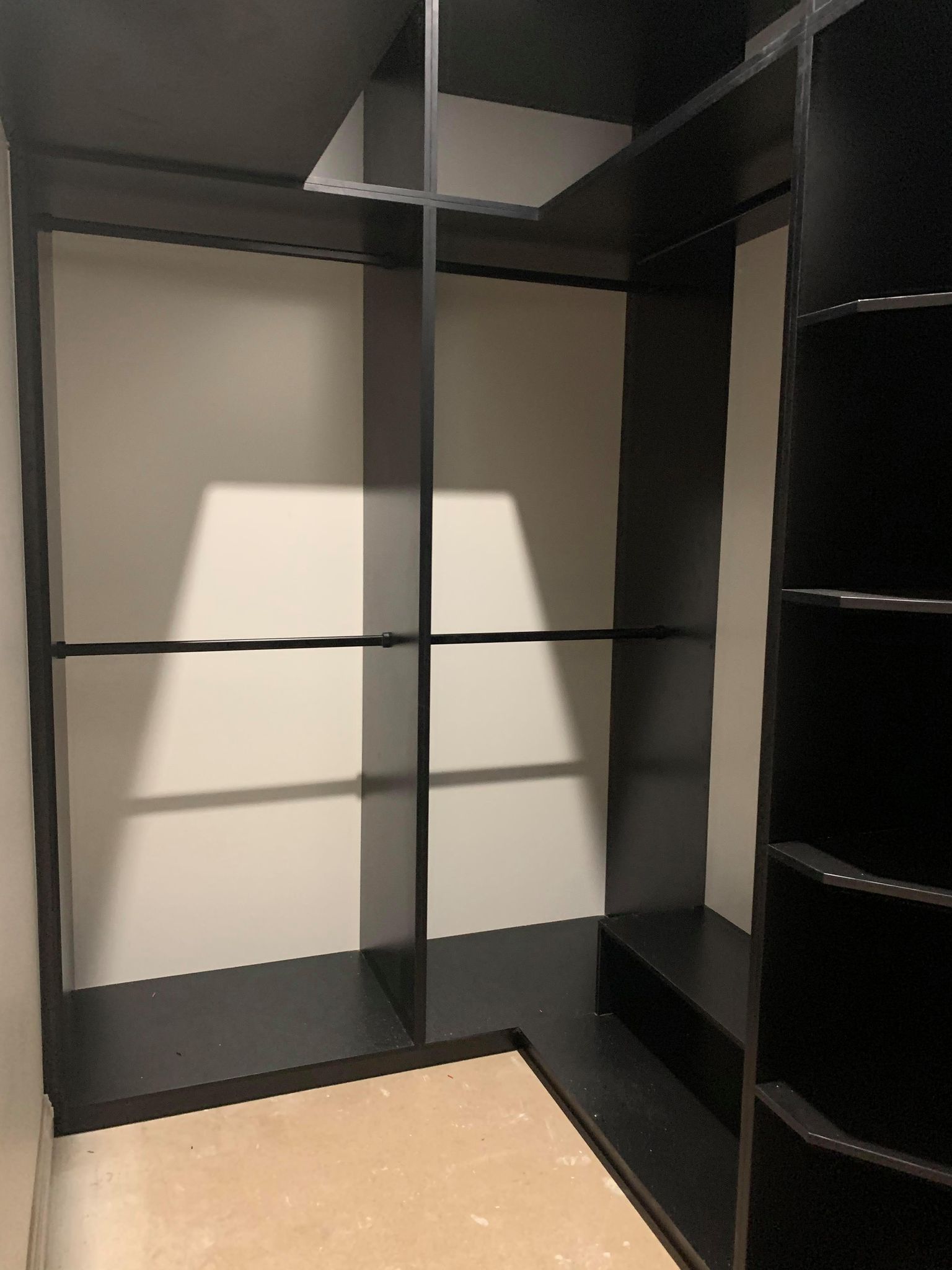 Empty black closet with shelves and hanging rods, beige walls, and tan floor.