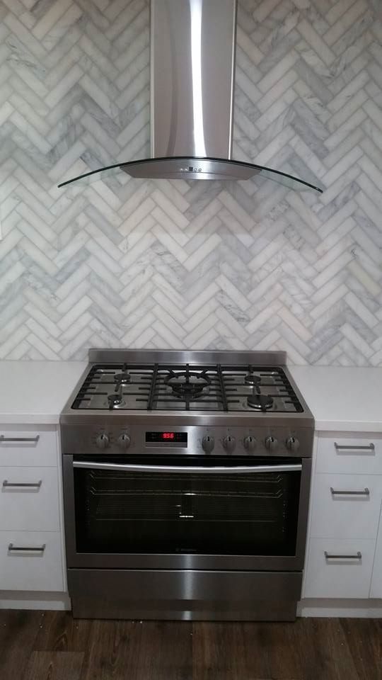 Stainless steel oven and range hood against a herringbone tiled backsplash in a kitchen.