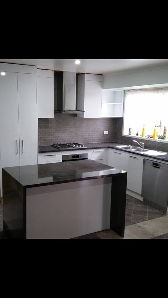 Modern white kitchen with a dark countertop island. Stainless steel appliances and a tile backsplash.