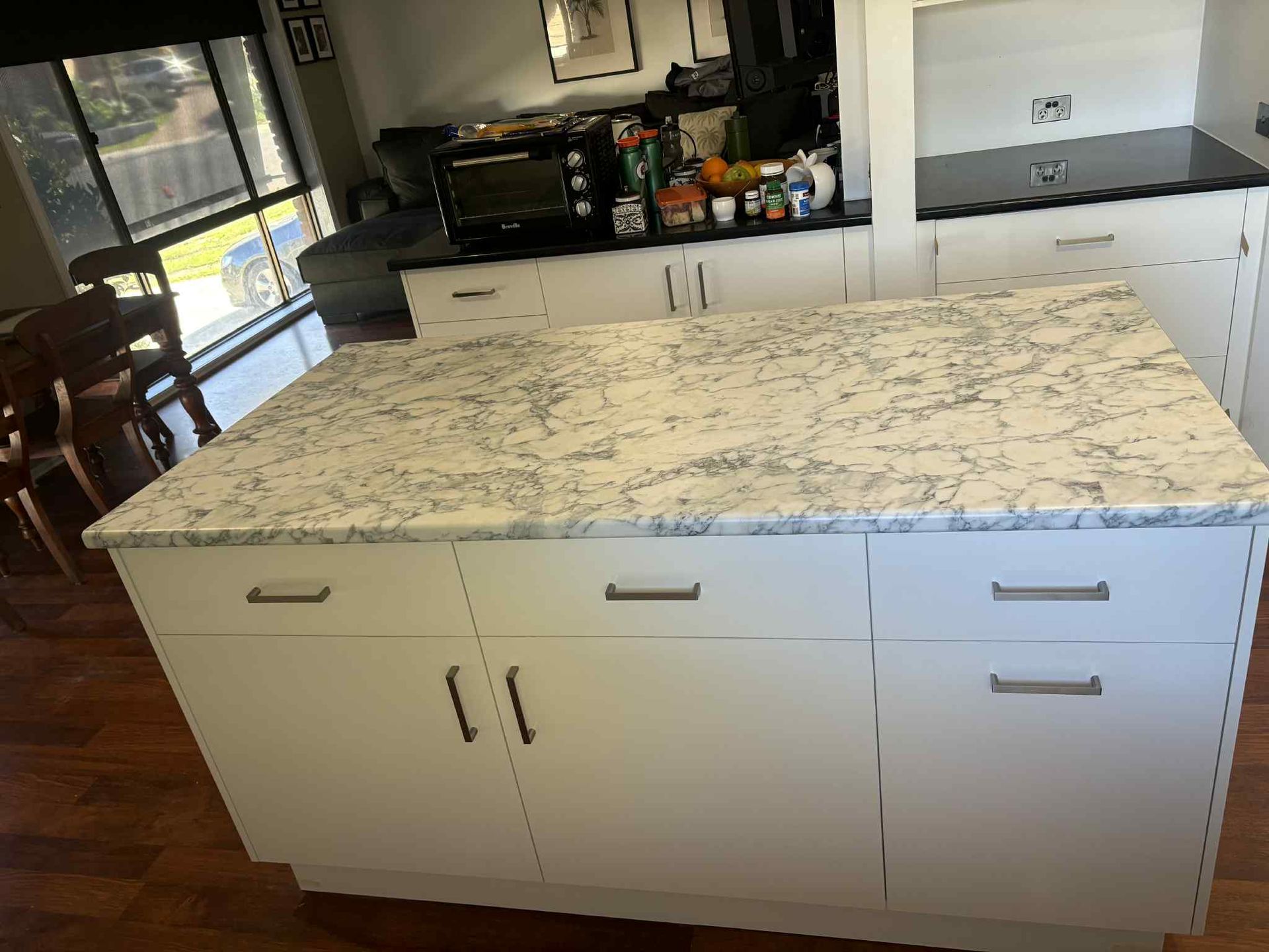 White kitchen island with marble countertop; surrounding cabinets, dark countertop.