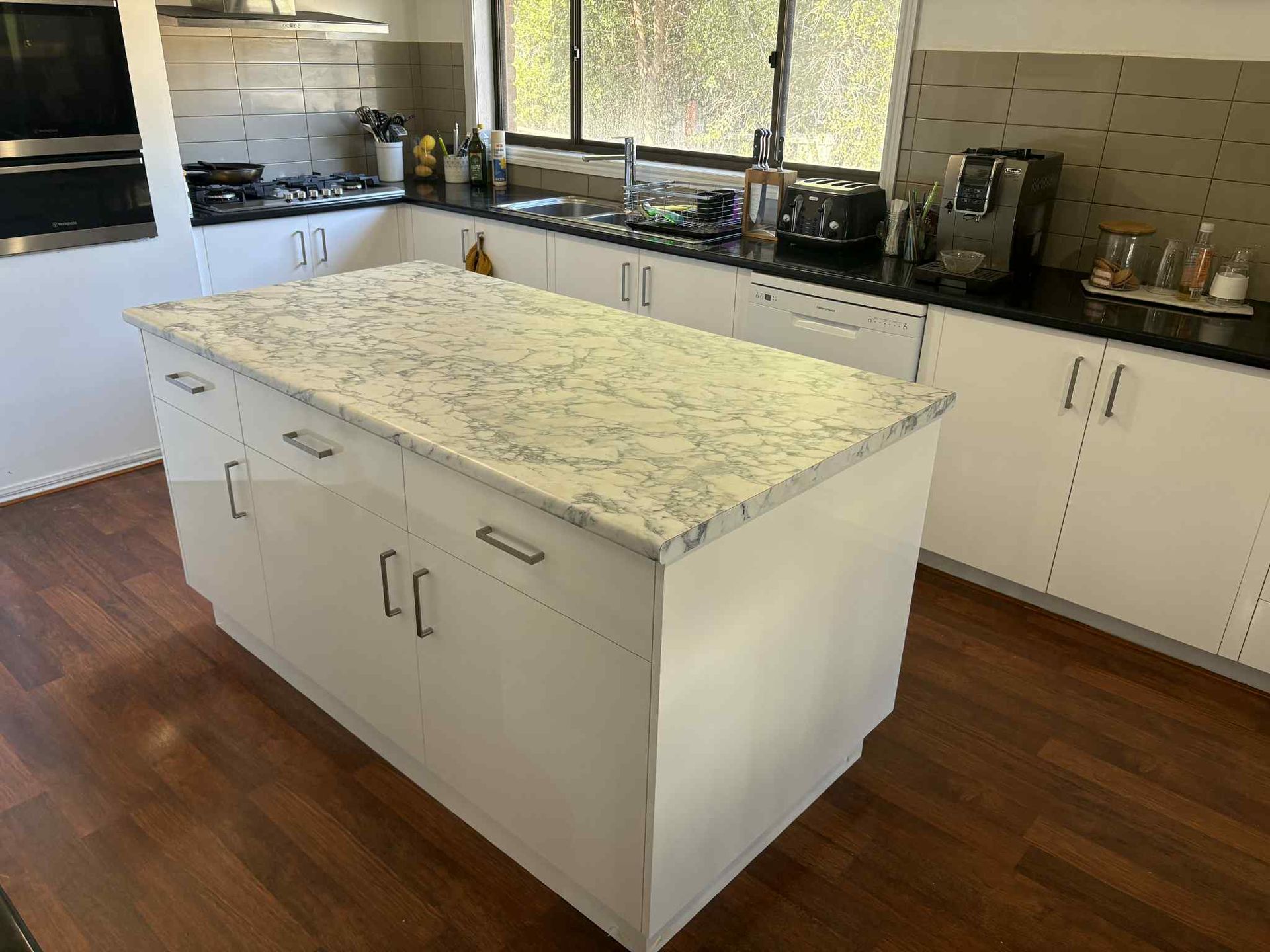 White kitchen island with a marble countertop in a kitchen with white cabinets.