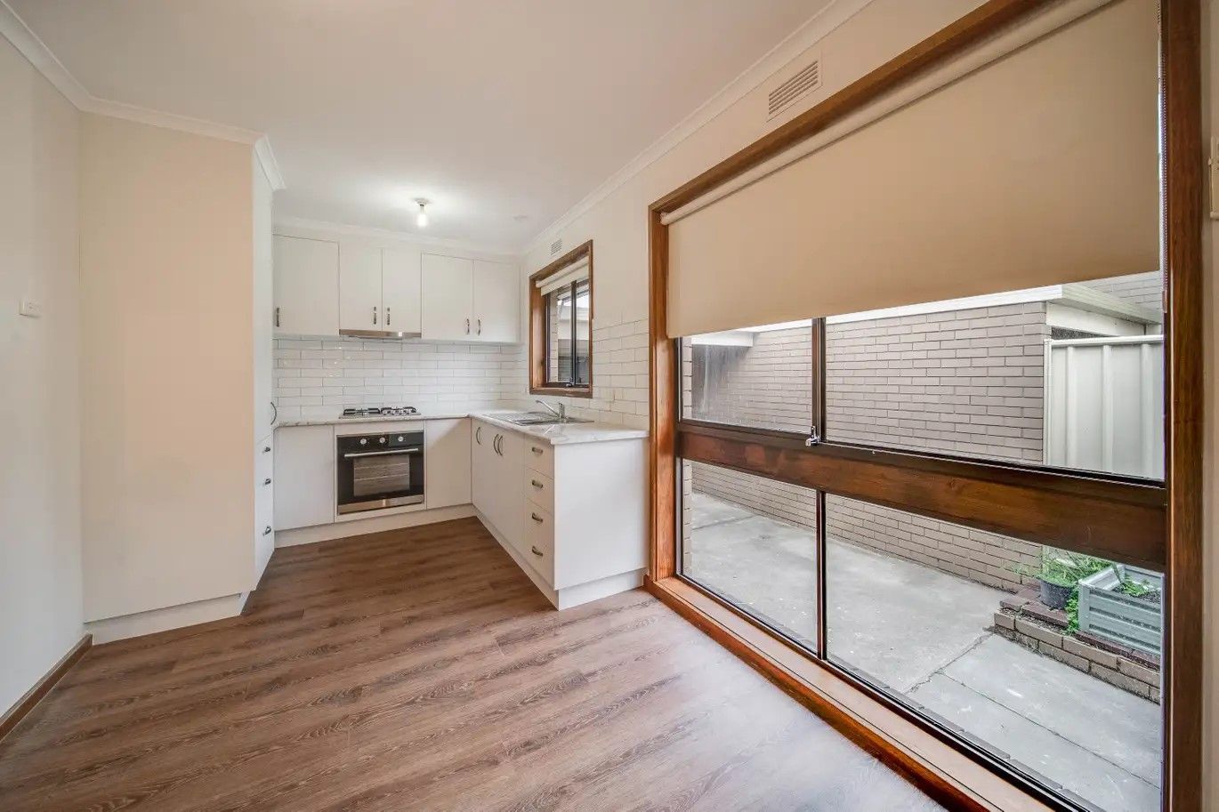 Kitchen with white cabinets, dark wood-look floor, large window with shade, and view of a small courtyard.