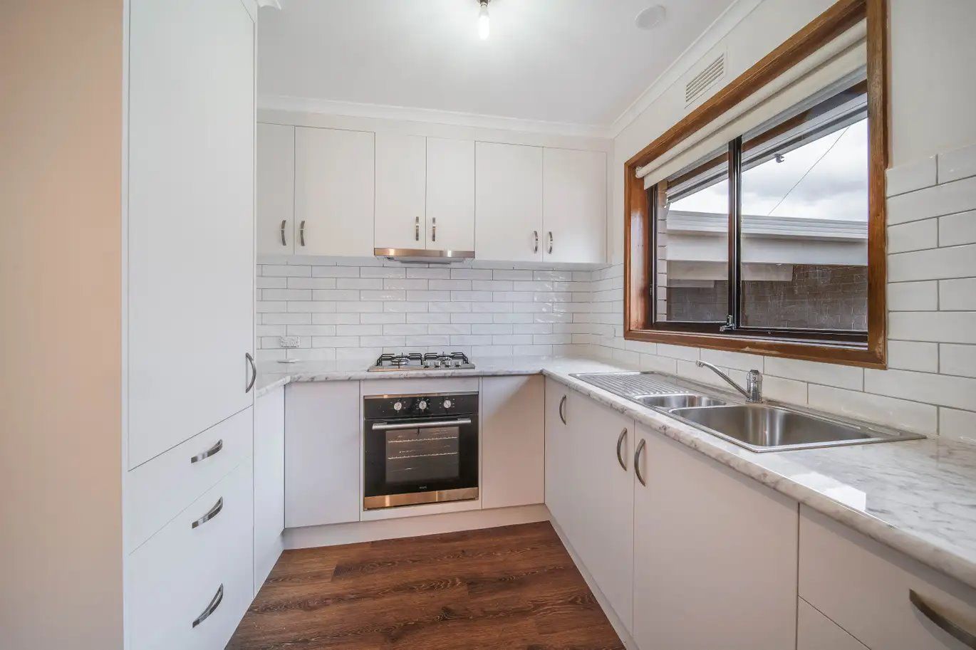 White kitchen with cabinets, oven, stove, sink, and a wooden window frame.
