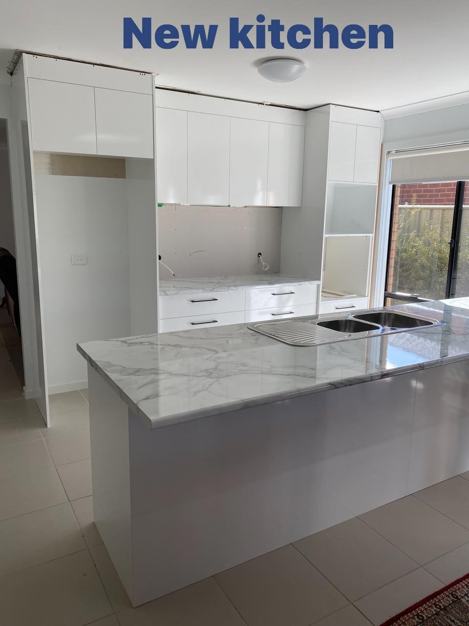 New white kitchen with marble countertops and a large island.
