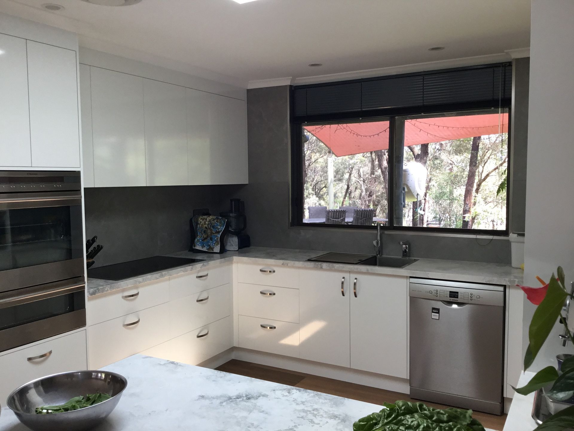 White modern kitchen with a large window overlooking a forest.
