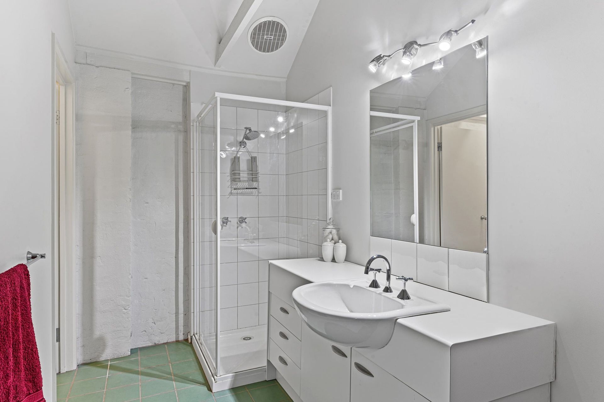 Bathroom with a white vanity, shower stall, and a red towel on the door. The floor is green.