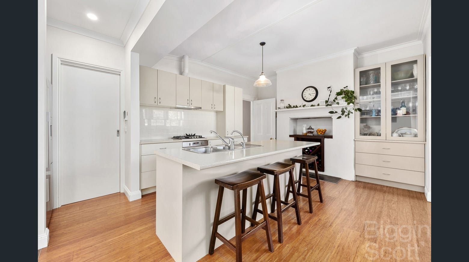 Kitchen with white cabinets, island with stools, hardwood floors, and a glass-fronted cabinet.