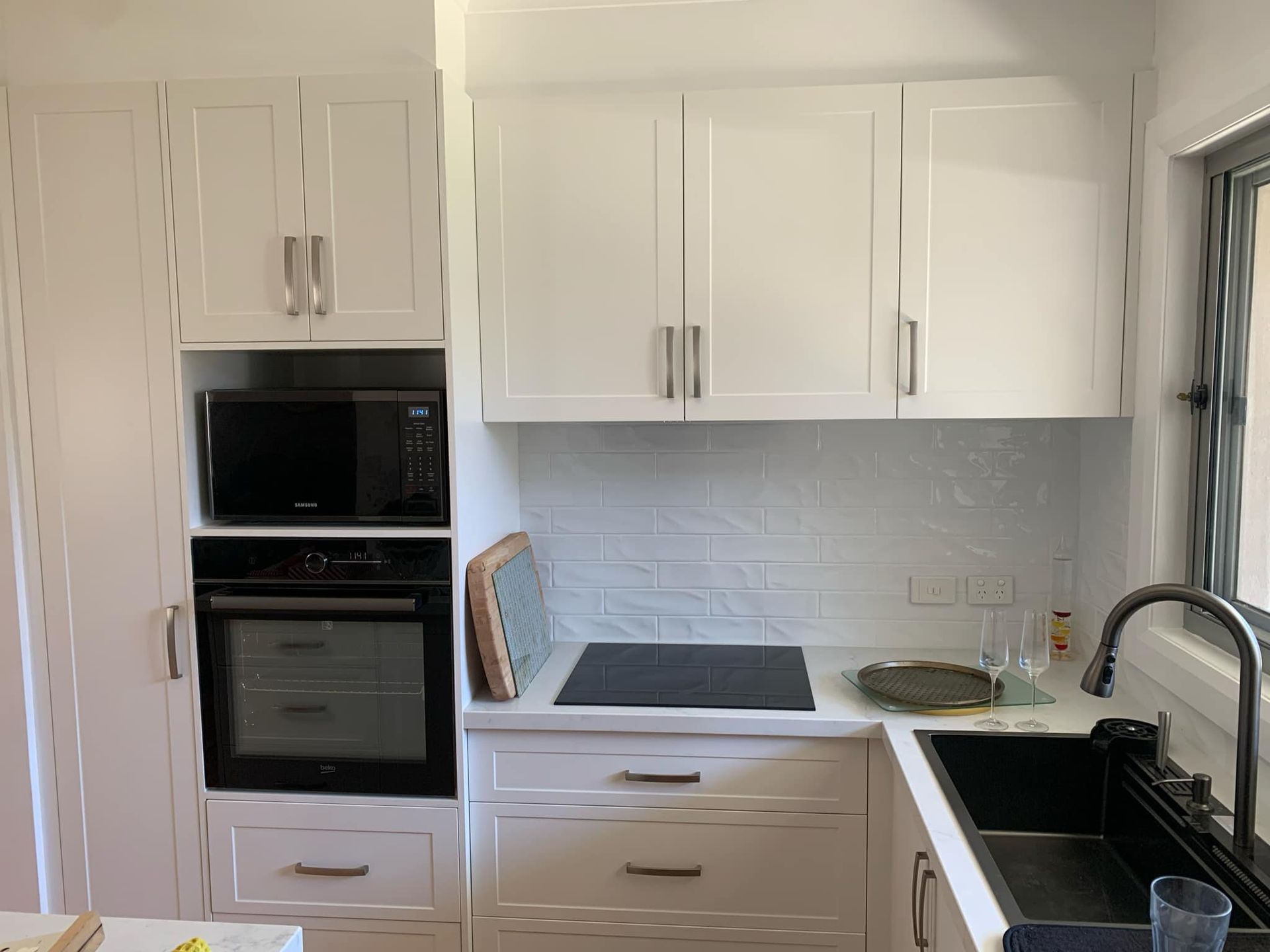 White kitchen with cabinets, oven, microwave, cooktop, and sink.