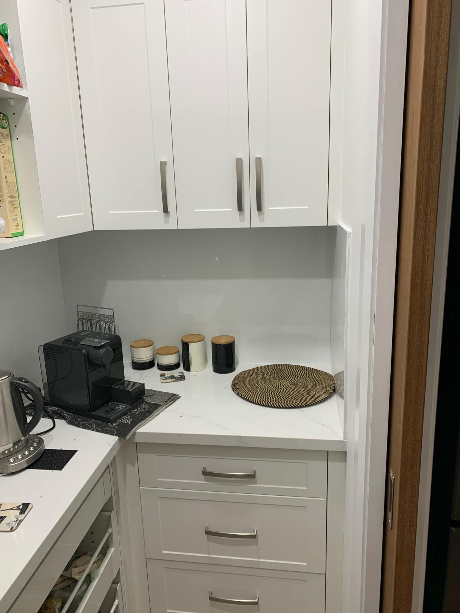 White built-in kitchen cabinets with countertop and coffee station, featuring drawers and decorative items.