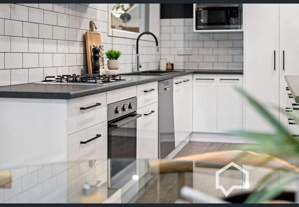 Modern white kitchen with black countertops, appliances, and hardware.