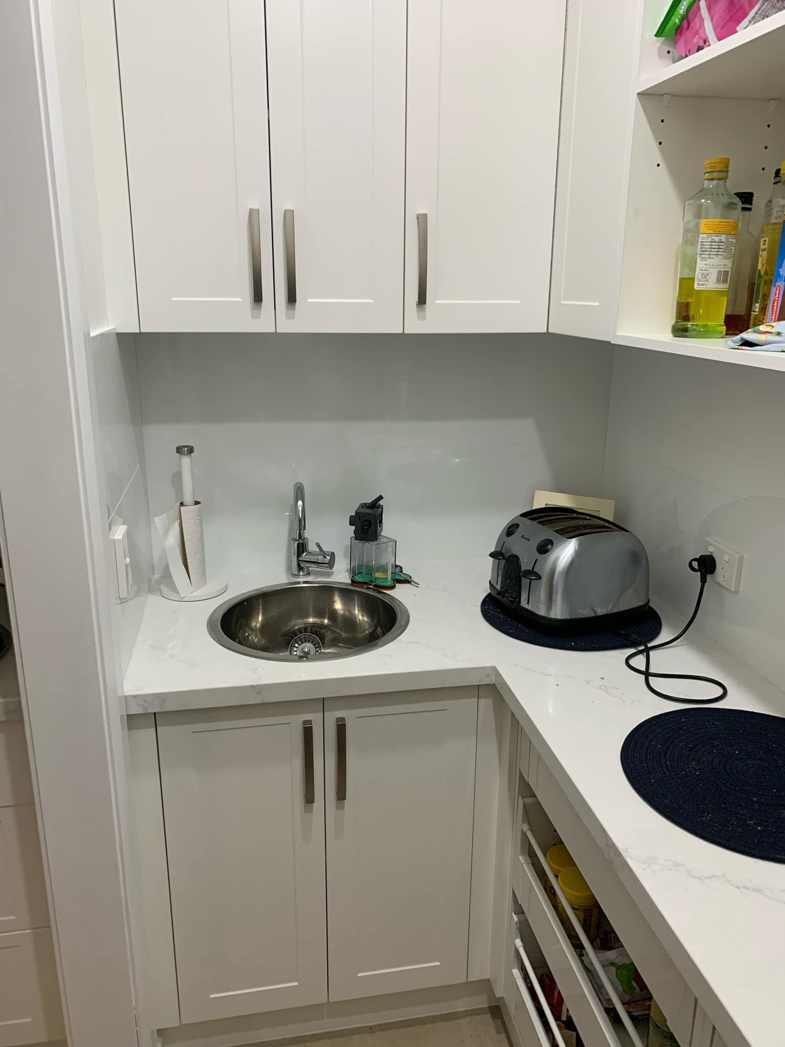 White pantry with sink, countertop, cabinets, toaster, and shelves.